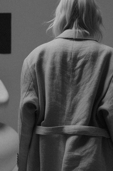 Black and white photo of a woman in a trenchcoat walking away.